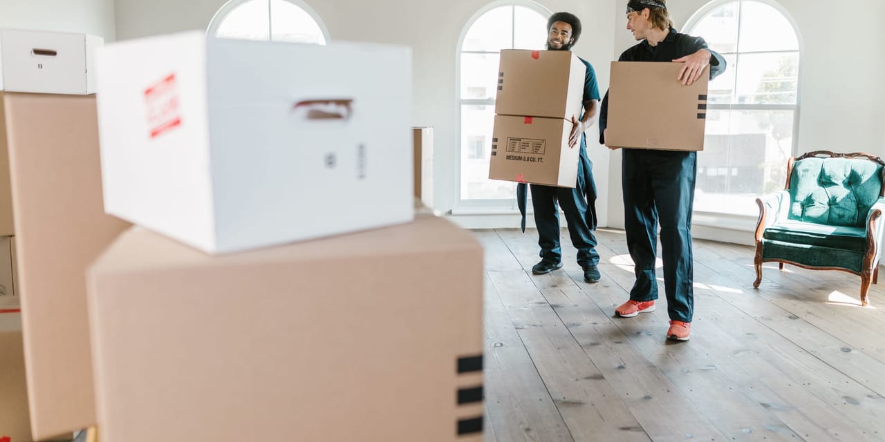 Zwei Mitarbeiter von EntrümpelBlitz in Arbeitskleidung tragen Umzugskartons durch einen hellen, leer geräumten Raum