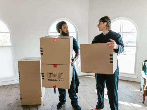Zwei Mitarbeiter tragen Umzugskartons durch einen hellen Raum